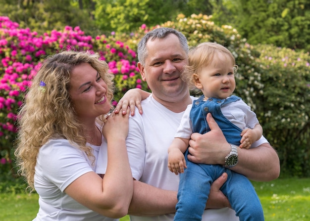 La mamma è in piedi accanto al papà che tiene tra le braccia un bambino di un anno con i capelli biondi Famiglia