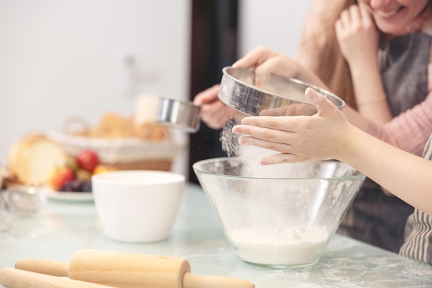 La mamma e la figlia dei suoi bambini più piccoli in una cucina moderna celebrano l'apprendimento gioioso della decorazione della torta di cottura felice piccola figlia preparano dolci con la mamma premurosa nel fine settimana a casa