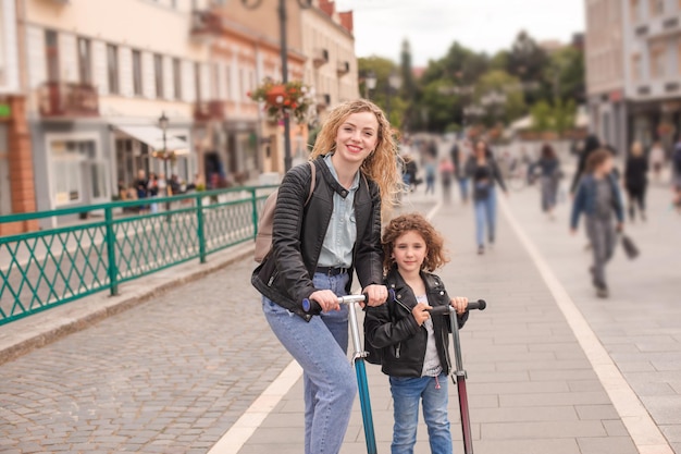 La mamma e la figlia felici sono in piedi con gli scooter in città