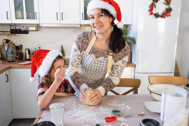 La mamma e la figlia nella cucina bianca stanno preparando biscotti per Natale e Capodanno La preparazione della giornata di famiglia per la festa Imparare a cucinare deliziosi pasticci tagliati in forme di pasta con stampi