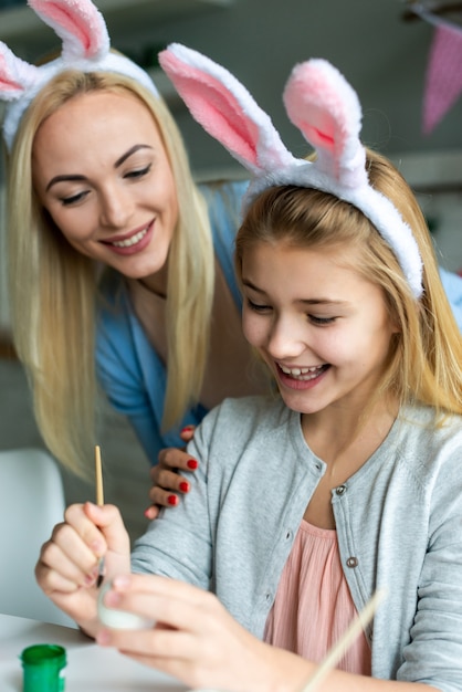 La mamma e la figlia sorridenti dipingono le uova di Pasqua in orecchie del coniglietto.