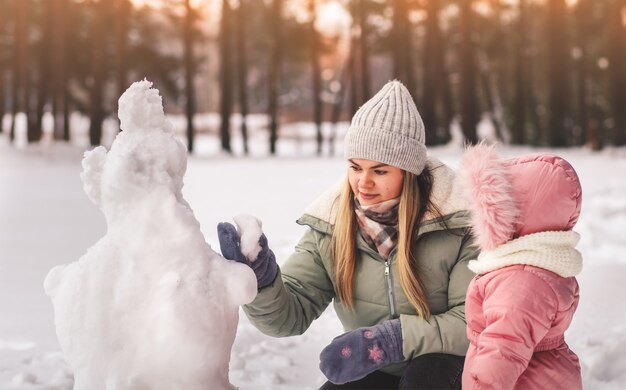 La mamma e la piccola figlia scolpiscono il pupazzo di neve in inverno nel parco