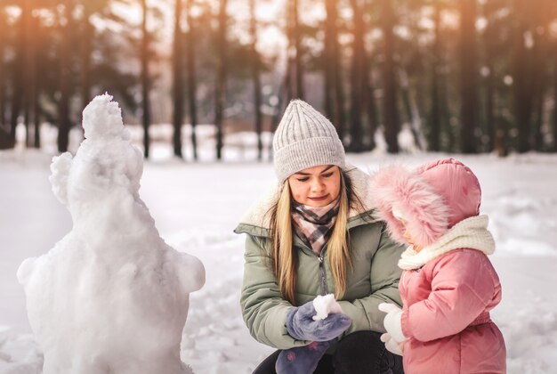 La mamma e la piccola figlia scolpiscono il pupazzo di neve in inverno nel parco