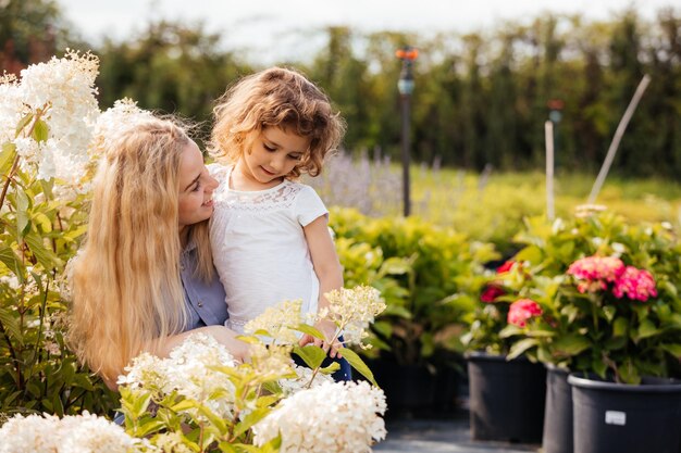 La mamma e la ragazza carina scelgono le piante per il loro giardino nel negozio di giardinaggio all'aperto