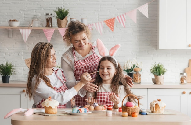 La mamma e le figlie di famiglia felice stanno giocando in cucina a dipingersi a vicenda con le vernici mentre si preparano per le vacanze di Pasqua.