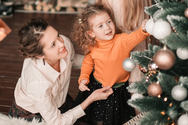 La mamma e le sue piccole figlie decorano l'albero di Natale. concetto di vacanza