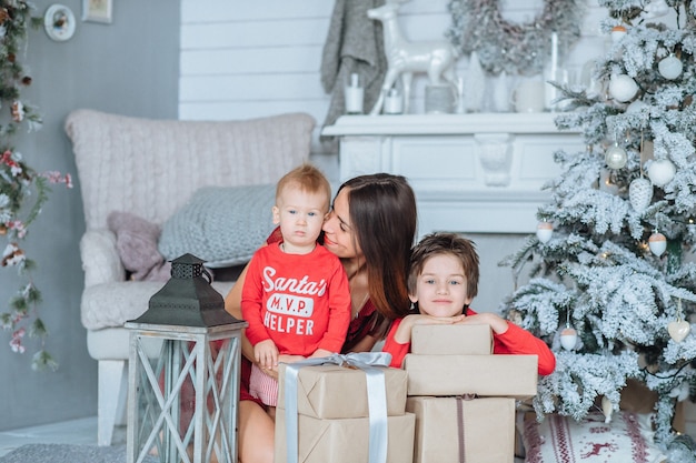 La mamma ei suoi due figli, vestiti di Capodanno, trascorrono del tempo all'albero di Natale, lo vestono, si divertono