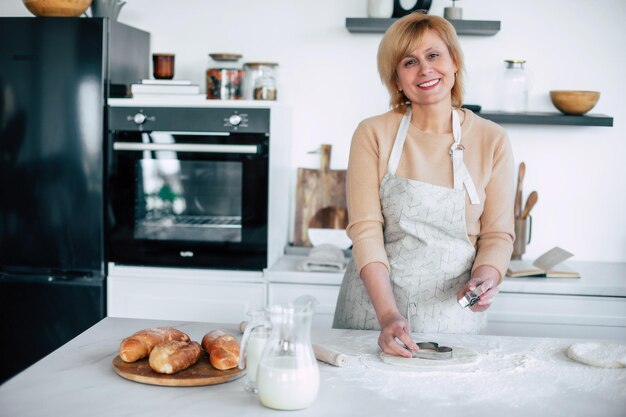 La mamma fa i biscotti Una bella donna sorridente e matura lavora con la farina di grano quando fa un impasto e prepara pasticci nella cucina moderna a casa Cucina cuoco a casa