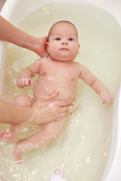 La mamma fa il bagno al suo bambino in una vaschetta di plastica bianca