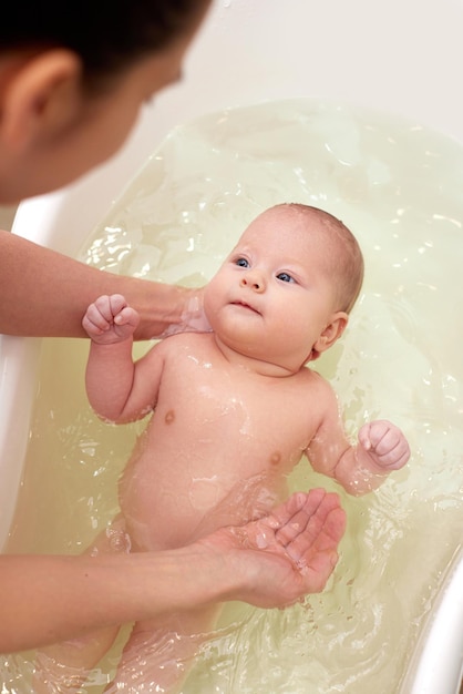 La mamma fa il bagno al suo bambino in una vaschetta di plastica bianca
