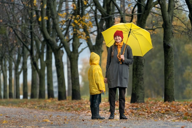 La mamma felice con l'ombrello giallo e il figlio con l'impermeabile giallo stanno in un parco autunnale Giornata piovosa