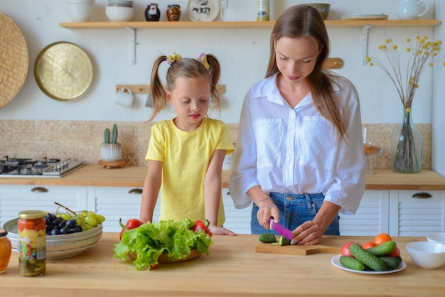 La mamma felice insegna alla piccola figlia a cucinare cibo sano mamma e ragazza che parlano sorridendo