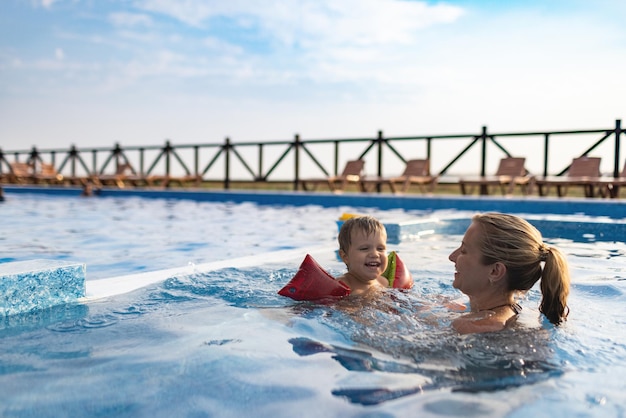 La mamma gioca con suo figlio con le maniche in piscina in estate