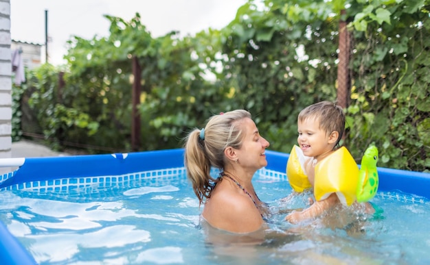 La mamma gioca con un bambino nudo in maniche corte in piscina sullo sfondo di un tramonto estivo