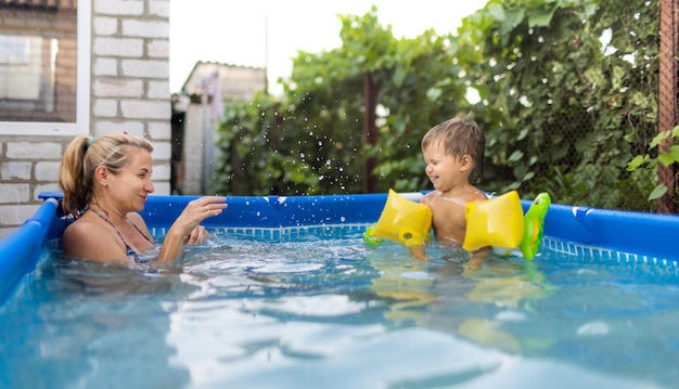 La mamma gioca con un bambino nudo in maniche corte in piscina sullo sfondo di un tramonto estivo