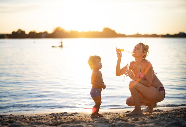 La mamma in bikini gioca con il bambino che soffia bolle godendosi le vacanze