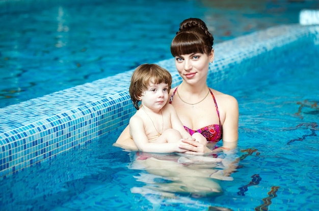 La mamma insegna a un bambino a nuotare in piscina.