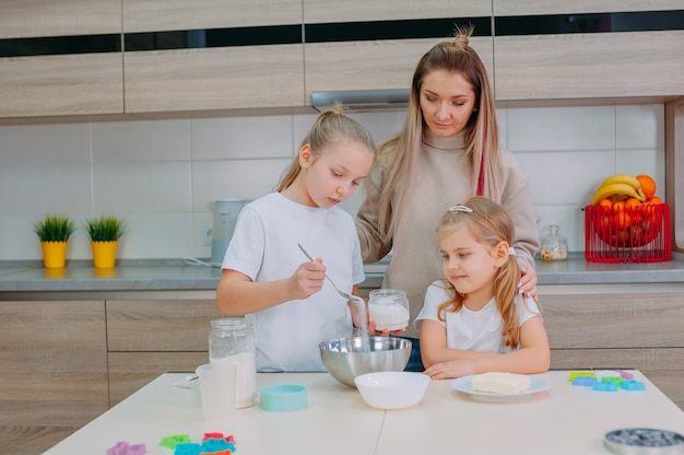 La mamma insegna alle sue figlie a cucinare la pasta in cucina.