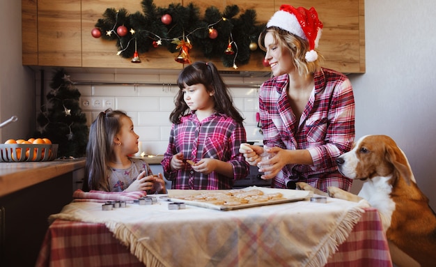 La mamma insieme alle sue figlie e al suo amato cane preparano biscotti allo zenzero e si divertono in cucina. preparazione per il Natale. Tradizione familiare.