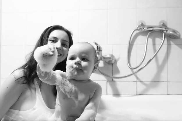 La mamma lava i bambini Mamma e bambini stanno prendendo le procedure dell'acqua nel bagno Spray schiuma