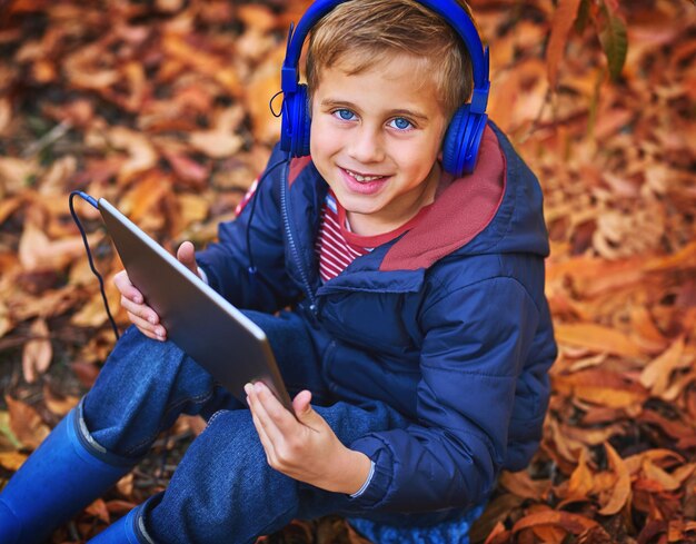 La mamma mi ha detto di giocare all'aperto Ritratto ad alta angolazione di un adorabile ragazzino che usa un tablet mentre è seduto all'aperto durante l'autunno
