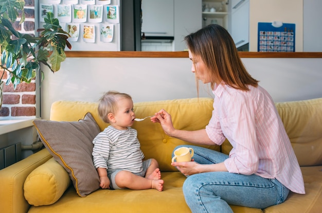 La mamma nutre un bambino piccolo a casa con lo yogurt da un concetto di famiglia di cucchiai