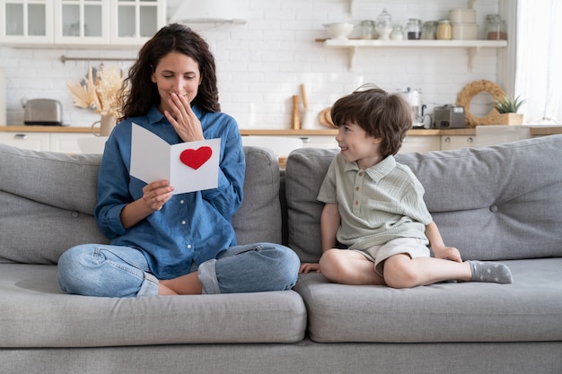 La mamma positiva legge i saluti dal biglietto fatto dal figlio del bambino in età prescolare alla festa della mamma o all'evento di compleanno birthday