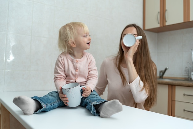 La mamma premurosa felice e la ragazza bionda bevono latte in cucina.