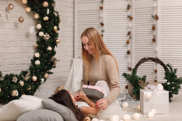 La mamma regala una confezione regalo a una bambina carina per Natale a casa