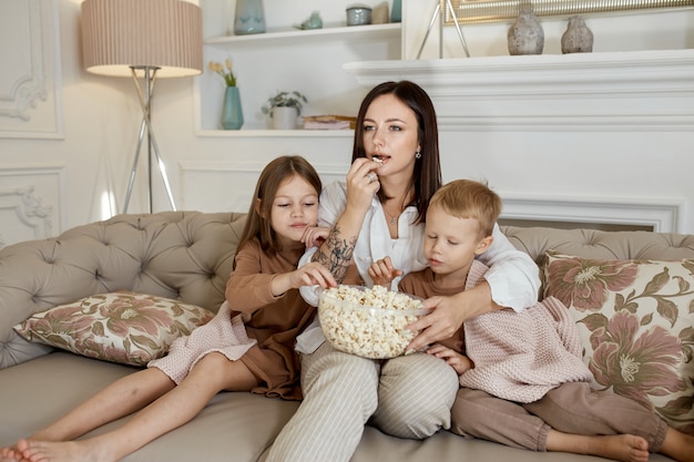 La mamma si siede sul divano con suo figlio e sua figlia e guarda un film