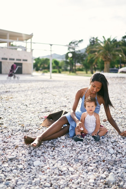 La mamma si siede sulla spiaggia e porge un sassolino a una bambina