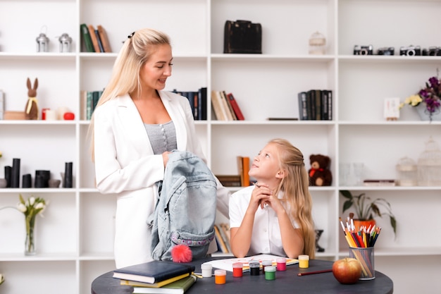 La mamma sorride a sua figlia, tiene uno zaino in mano, raccoglie sua figlia a scuola