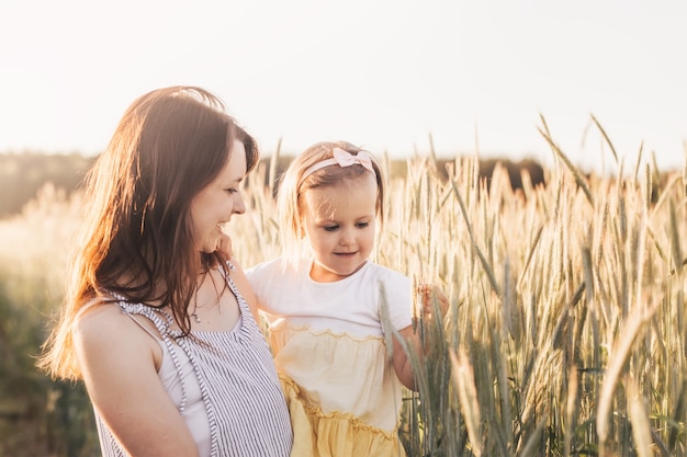 La mamma tiene in braccio la sua piccola figlia in un campo di grano in estate