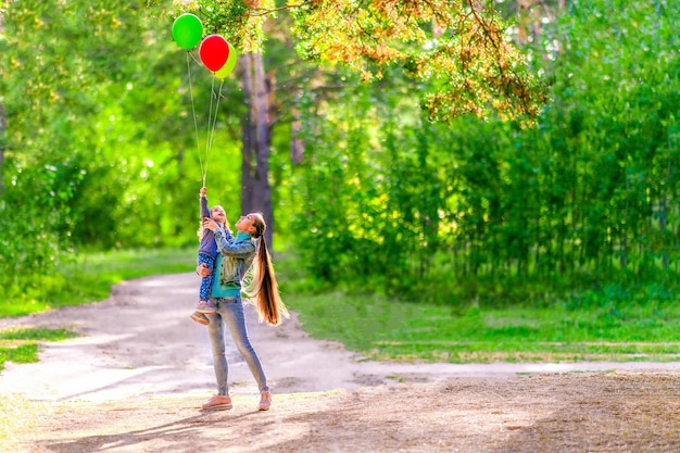 La mamma tiene in braccio sua figlia mia figlia tiene in mano palloncini Passeggiata nella foresta estiva Giornata di sole splendente