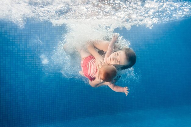 La mamma tiene la figlia immersa nell'acqua che nuota sott'acqua nella piscina per bambini Immersione del bambino Imparare il bambino a nuotare Giovane madre o istruttore di nuoto e bambina felice