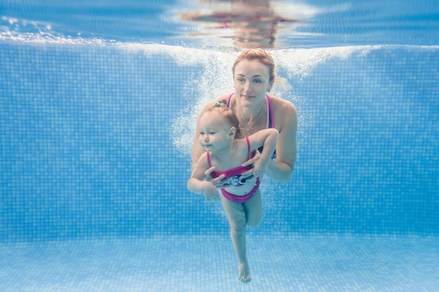 La mamma tiene la figlia immersa nell'acqua, nuota sott'acqua nella piscina per bambini. Bambino subacqueo. Imparare a nuotare. Giovane madre o istruttore di nuoto e bambina felice.