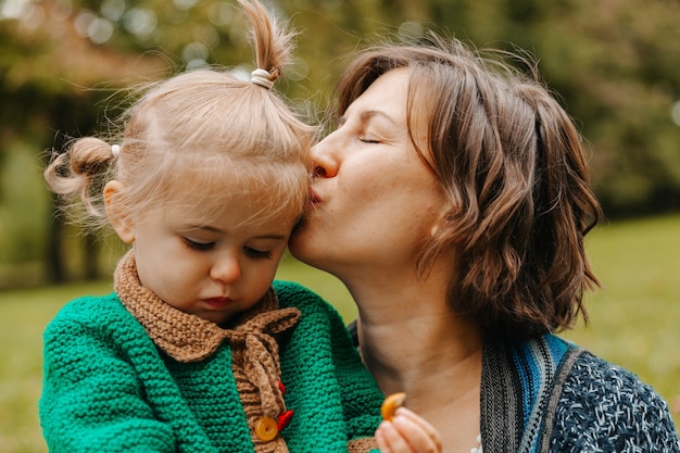 La mamma tiene la figlia tra le braccia nel parco. donna con un bambino piccolo sta camminando nel parco autunnale. autunno.