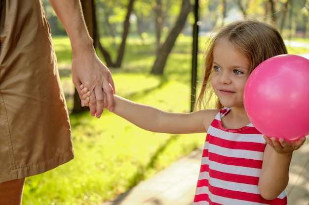 La mamma tiene la mano di una bambina con un palloncino nel parco