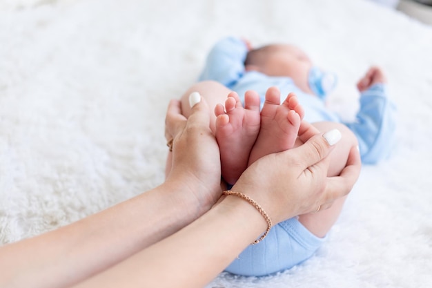 La mamma tiene le gambe di un neonato tra le mani su uno sfondo bianco da vicino, l'amore e la cura della mamma