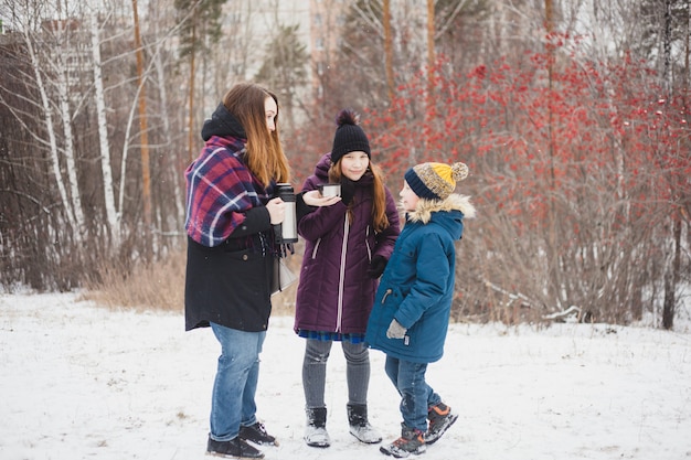 La mamma versa il tè caldo o beve da thermos per sua figlia e suo figlio, passeggiata invernale, inverno