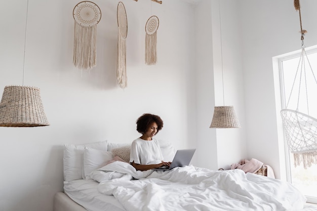 La manager delle ragazze africane con laptop ha una riunione video online con colleghi e partner commerciali in un letto accogliente a casa al mattino Tendenze e attività della discussione di squadra