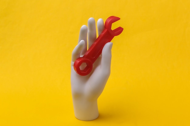 La mano bianca del manichino tiene la chiave su sfondo giallo. Concetto di ristrutturazione, industria. minimalismo