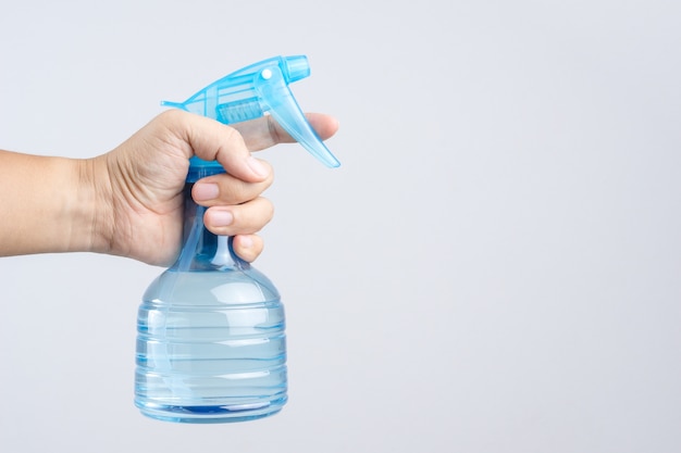 La mano che tiene il flacone spray di plastica blu contiene acqua pura