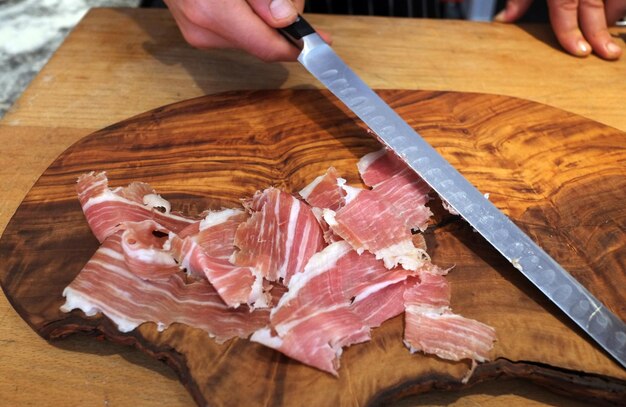 La mano che tiene un coltello con la carne sul tavolino da tagliare