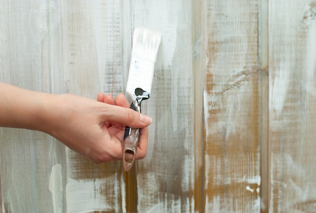 La mano con la spazzola dipinge la parete di legno nel bianco