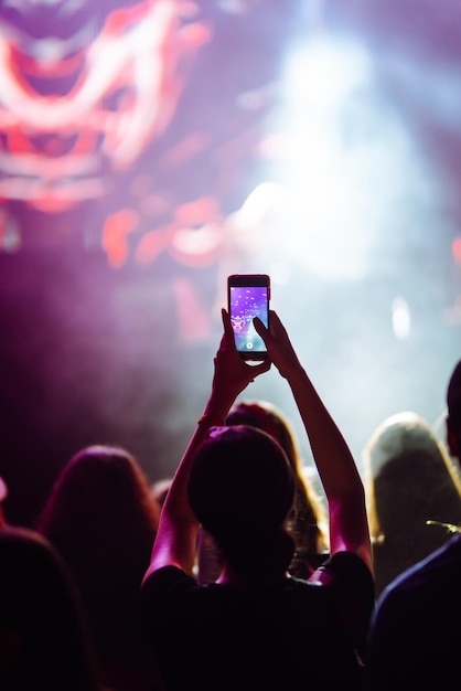 La mano con un telefono registra un festival di musica dal vivo Le persone scattano fotografie con lo smartphone