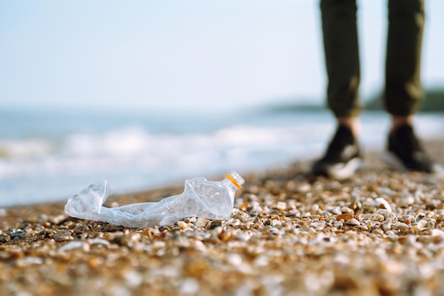 La mano degli uomini raccoglie la bottiglia di plastica sulla spiaggia del mare. Il volontario che indossa guanti protettivi raccoglie la bottiglia di plastica.