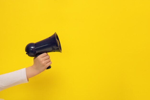 La mano dei bambini che tiene un megafono su uno sfondo giallo con spazio per la copia