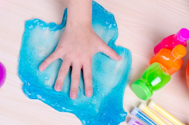 La mano del bambino ha fracassato una melma blu brillante sul tavolo. Immagine dall'alto verso il basso della mano del bambino e degli slime, giocattolo popolare in tutto il mondo.