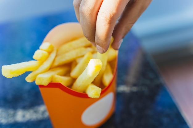 La mano del bambino prende delle deliziose patatine fritte dorate da una tazza di carta.